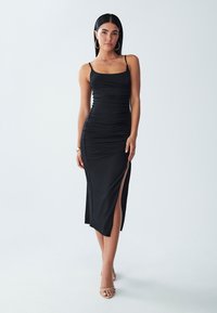 Black sleeveless dress with ruched texture, mid-calf length, and side slit. Smooth fabric, fitted design, and minimalistic style.
