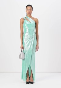 Mint green one-shoulder dress in shiny fabric with drapery and front slit; complemented by a silver handbag and black heels.