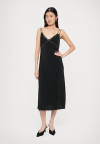 Vestido de cetim preto com alças finas, apresentando um detalhe geométrico de contas ao longo do decote e uma silhueta fluida em linha A.