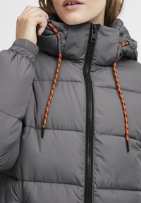Gray puffer jacket featuring a zippered front, elastic cuffs, and adjustable orange drawstrings on the hood. Textured, quilted pattern.