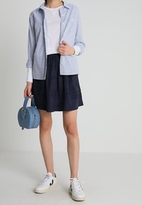 Camicia a righe blu e bianche sopra una maglietta bianca, abbinata a una gonna blu marina e scarpe da ginnastica bianche. Piccola borsa rotonda blu come accessorio.