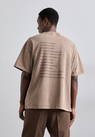 Camiseta marrón de gran tamaño con mangas cortas y líneas de texto impresas en la parte trasera. Confeccionada en tejido suave, con cuello redondo y dobladillo recto.