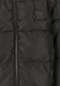 Sort puffer-jakke med quiltede sektioner, en frontlynlås, justerbare snore og et gummi-logo-patch på brystet.