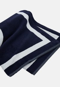 Marineblaue Handtuch mit dicken weißen Streifen, weicher Textur, rechteckiger Form und einem gesäumten Rand, der einen kontrastierenden Stoffdetail zeigt.