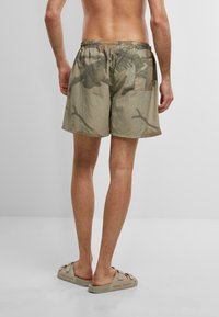 Pantaloni corti in lino con un motivo mimetico, toni di grigio e beige, con vita elastica e tasca posteriore. Indossati con sandali beige.