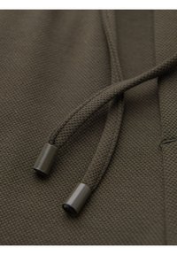 Gros plan sur un tissu brun foncé texturé avec deux cordons épais terminant par des embouts en plastique lisse.