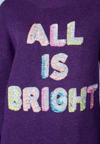 Pull en tricot violet avec des lettres multicolores en sequins formant l'inscription "ALL IS BRIGHT." Encolure côtelée et texture douce.