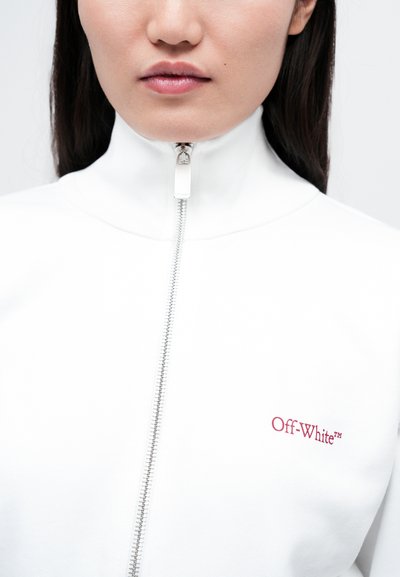 Giacca bianca con zip con colletto alto, zip argentata e piccolo logo rosso "Off-White™" sul lato sinistro del petto. Texture liscia.