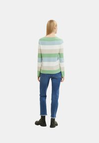 Gestreifter Pullover in Grün, Blau und Beige, mit Rundhalsausschnitt und langen Ärmeln, kombiniert mit blauen Jeans und schwarzen Stiefeletten.