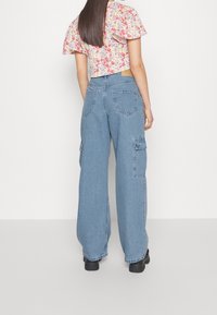 Jeans cargo de pierna ancha en denim azul claro con dos bolsillos laterales y bolsillos traseros. Textura suave con un diseño de ajuste holgado.