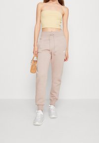 Ljusbeige joggingbyxor med cuffs i anklarna och dragsko i midjan; kombinerade med en gul strapless topp och grå-vita sneakers. Litet logotyp från varumärket på byxorna.