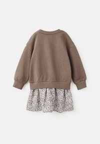 Hanorac maro cu umeri lăsați și manșete țesute, prezentând o fustă în carouri cu imprimeu de leopard în nuanțe de gri și alb dedesubt.