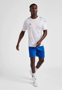 Herre atletisk outfit, der omfatter en hvid kortærmet trøje med blå accenter og logo, kombineret med blå shorts. Båret med hvide sokker og sko.