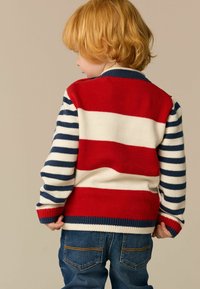 Knit sweater featuring horizontal red, white, and navy stripes, with a solid red back and ribbed cuffs; paired with blue denim jeans.
