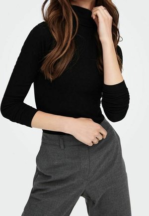 Sort, ribstrikket rullekrave-top med lange ærmer kombineret med grå, skræddersyede bukser. Stoffet virker strækbart med en tætsiddende silhuet.