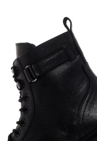 Stivale alla caviglia in pelle nera con finitura testurizzata, punta rotonda, design con lacci e una fascia laterale con hardware in metallo.