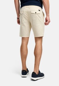 Beige katoenen shorts met een slim fit, vlakke voorkant en twee achterzakken. Draag ze met marineblauwe sneakers met witte zolen.