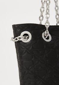Geantă de umăr neagră cu un model geometric texturat, având accesorii argintii și o curea din lanț, îmbinând un design elegant cu o formă structurată.