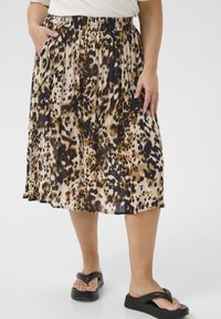 Jupe midi à imprimé léopard avec une taille élastique, en tissu léger, poches latérales et design fluide. Portée avec des sandales noires à lanières.