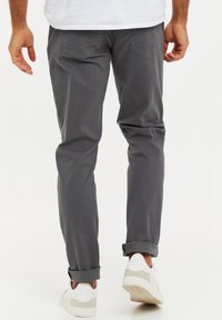 Szare bawełniane spodnie o slim fit, z tylnymi kieszeniami i podwiniętymi mankietami, w połączeniu z białymi sneakersami.