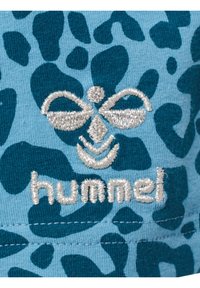 Turkos tyg med ett mörkblått leopardmönster; har en silverbroderad logotyp med en stiliserad bi och ordet "hummel."