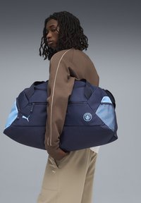 Bolsa de deporte marina con acentos en azul claro, que cuenta con dobles cremalleras, parche de logo y panel lateral de malla texturizada. Fabricada con un tejido duradero.