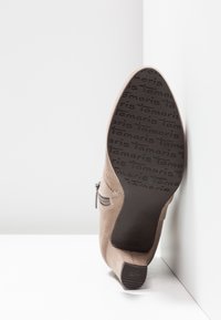Bottine en daim beige avec talon bloc, détail zippé et motif de la marque "Tamaris" sur la semelle ainsi que sur l'embout antidérapant du talon.