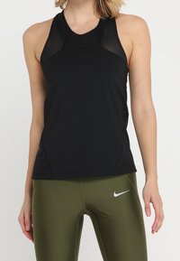 Czarny sportowy top na ramiączkach z przezroczystymi panelami z siateczki, dopasowany fason i okrągły dekolt; w zestawie z oliwkowozielonymi dopasowanymi legginsami z białym logo.