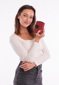 Red textured wallet with a black clasp, held in a hand. The wallet is rectangular with rounded edges and visible stitching details.