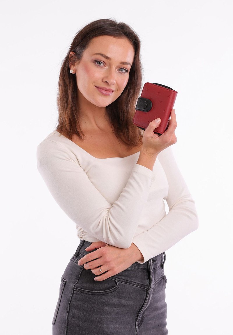 Red textured wallet with a black clasp, held in a hand. The wallet is rectangular with rounded edges and visible stitching details.