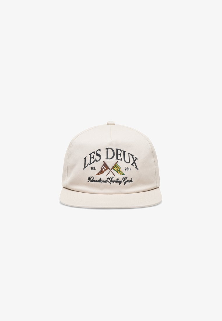 Beige cap with a flat brim, featuring embroidered "LES DEUX" text and crossed flags in brown and green. Made of fabric with a smooth texture.