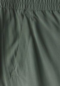 Ciemnozielony materiał z elastycznym paskiem w talii, gładką fakturą i boczną kieszenią z kanciastymi detalami ś stitching.