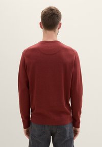 Piros, hosszú ujjas pulóver kerek nyakkal, bordás mandzsettákkal és szegéllyel, sima textúrával, hátulról nézve.