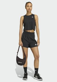 Czarny krótki top na ramiączkach i czarne szorty z elastycznym pasem. Czarne tenisówki z białymi paskami oraz brązowa torebka na ramię z wzorem.