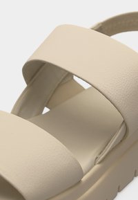 Μπεζ σανδάλι με δύο φαρδιές λουριά και μαλακή σόλα, σχεδιασμένο για άνεση με υφή φινιρίσματος.