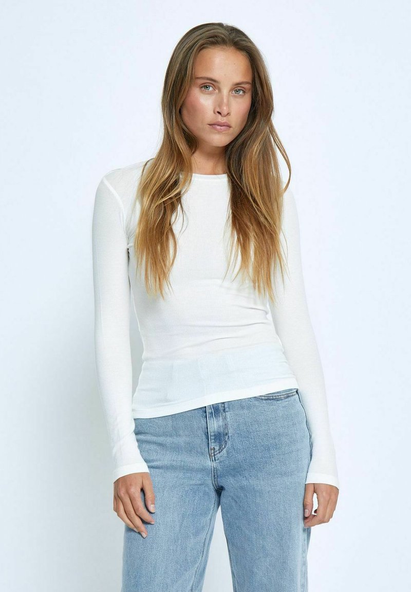 Witte lange mouwen ribbel top met een aansluitend ontwerp, voorzien van een ronde hals en langere manchetten, gecombineerd met lichtblauwe rechte jeans.