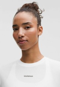 Valge T-särk ümmarguse kaelusega, millel on must "lululemon" logo, sile kangas ja sobiv disain õlgade ümber.