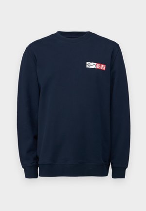 Sweatshirt bleu marine en tissu doux, avec un col rond, des manches longues et un patch logo blanc/rouge centré sur la poitrine.