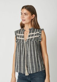 Lühikeste varrukatega blouse tumehallis värvimas, geomeetriliste valgete mustritega, volditud kangast ning võtmeaugu dekolteega, millel on pitsidega detail.