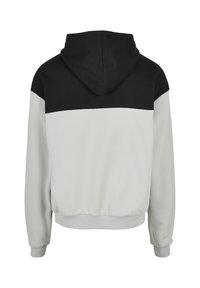 Sweat à capuche avec un panneau supérieur noir et un corps gris clair, fabriqué en tissu mélange de coton avec des poignets et un ourlet côtelés.