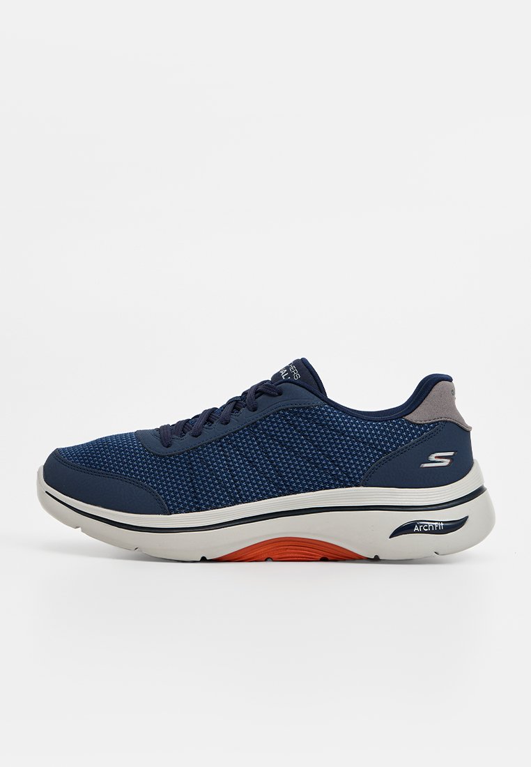 Zapatillas deportivas azul marino con un upper de malla transpirable, una media suela blanca gruesa y acentos en la suela naranja. Diseño con cordones y cuello acolchado.