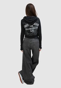 Czarna krótka bluza z kapturem z graficznym nadrukiem i prążkowaną fakturą, zestawiona z luźnymi, ciemnoszarymi jeansami. Bluza posiada duże kieszenie i szerokie nogawki.