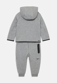 Sivi dukserica s kapuljačom i trenirke, izrađeni od mekanog materijala, s kapuljačom, crnim obrubima i detaljima s patentnim zatvaračem. Nike logo prikazan na oba komada.