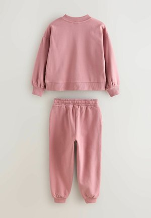 Sudadera larga de manga con un suave tono rosa, con puños acanalados, y pantalones de chándal de cintura elástica a juego, dispuestos de forma plana sobre un fondo claro.
