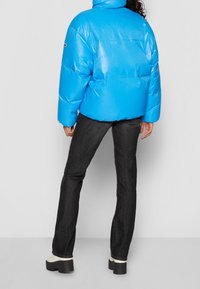 Blue puffer jacket with a high collar, shiny texture, and elastic hem, paired with dark jeans and chunky white-soled boots.