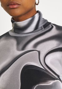 Grau und schwarze Rollkragen-Sweatshirt mit einem glatten, gewellten Muster, weicher Textur und taillierter Passform.