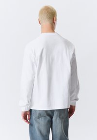 Langærmet hvid bomulds T-shirt med rund hals, afslappet pasform og blød tekstur, kombineret med lyseblå jeans.