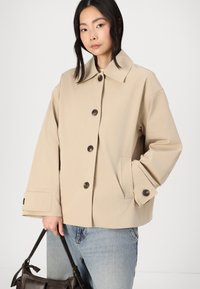 Beige bomulljakke med oversized passform, spiss krage og to store knapper. Har frontlommer og oppbrettede ermer for ekstra detaljer.