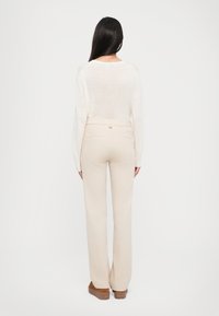 Pantalons beige clair, cintrés avec une taille haute et des poches arrière, associés à un haut en tricot crème à manches longues.