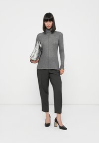 Pull col roulé gris avec une fermeture éclair sur le devant, associé à un pantalon gris foncé et des escarpins noirs. Pochette en cuir couleur serpent argenté.